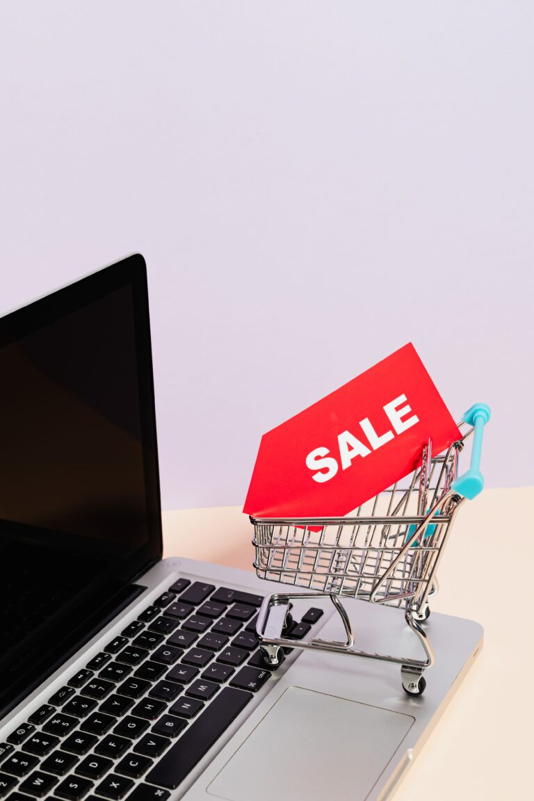 Mini shopping cart with a red sale tag resting on a laptop keyboard, representing online promo code savings