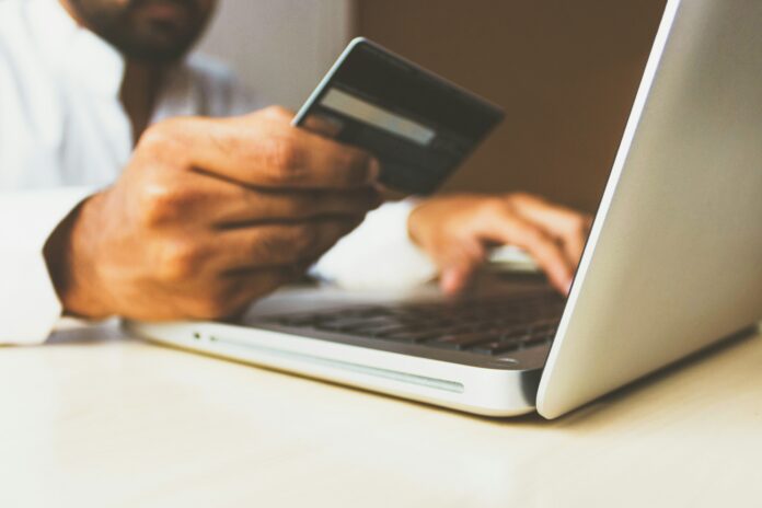 photo-1563013544-824ae1b704d3 Person holding a credit card while shopping online on a laptop, illustrating how cashback shopping works