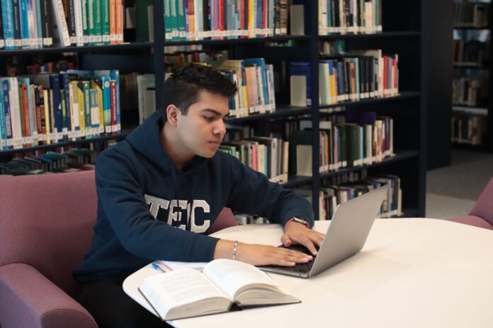 Student studying at a library desk with a 2-in-1 laptop and textbooks